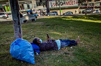 A homeless man lies on the grass in MacArthur Park in Los Angeles in May.