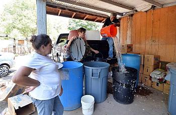 Juana Garcia, 49, watches as volunteers Donna Johnson, 72, center, and Ruben Perez, 68, deliver non-potable water to barrels on her back porch in East Porterville, California on June 4, 2015. Garcia, who suffers from lupus and arthritis, has difficulty lifting heavy objects and making the 15 minute walk with her children to a local church for showers several times a week. SILVIA FLORES sflores@fresnobee.com  