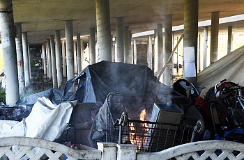 Homeless people wrap themselves in tarps as they try to keep warm near a fire at a homeless encampment beneath the El Dorado St