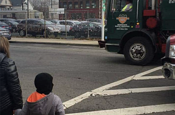 Trucks rumble along the road outside Hawkins Street School in Newark, New Jersey, as a family waits to cross.