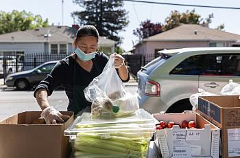 Norma Lazcano places potatoes in a bag at a food pick-up site at the Los Robles Ronald McNair Academy in East Palo Alto on May19