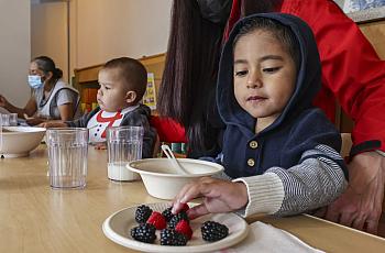 Adriel, 3, eats some berries with the other children whom child care provider Miren Algorri, standing, serves at her home.