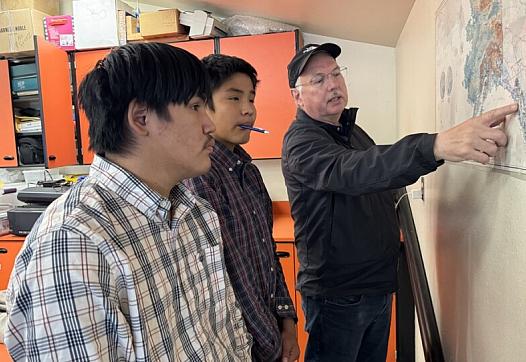 Person pointing to a map while speaking to 2 others