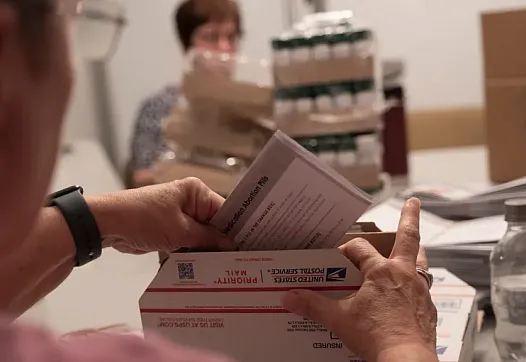 Volunteers at an abortion pill provider work around a conference table to pack 500 boxes to be sent to people in all 50 states. 