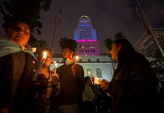People holding lit candles in evening with LGBTQ+ flag