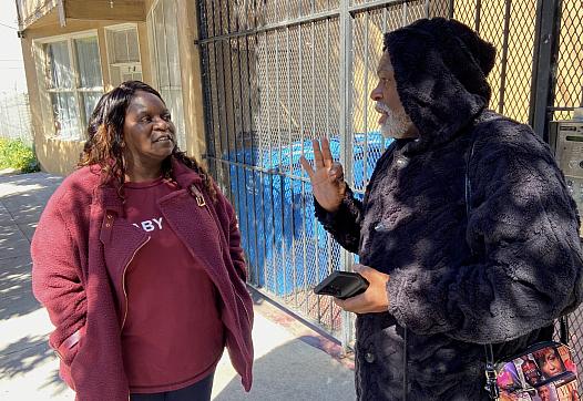 Two people talking, one wears a red top and another a black hoodie