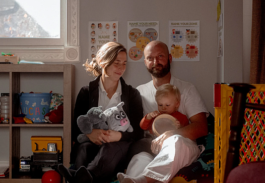 2 people sitting together, one with a child in their lap