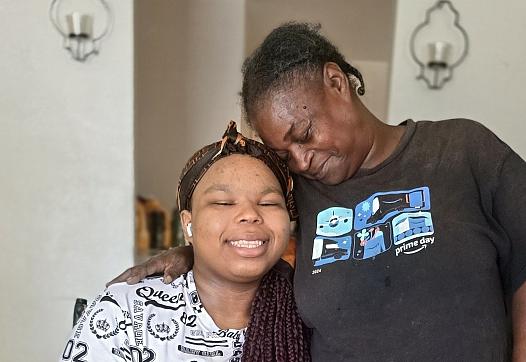 A Black woman embraces her granddaughter, who wears a prosthetic leg, in their Kern County home.