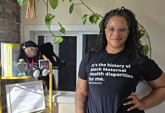 A young Black woman in glasses stands hand on hip inside a doula clinic