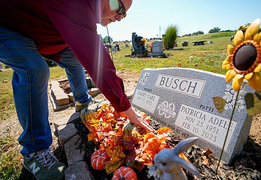 Person putting flowers on a toubstone