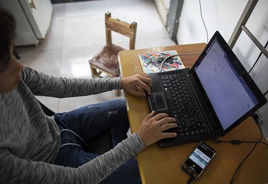 A girl on a laptop, with a cell phone on the table.
