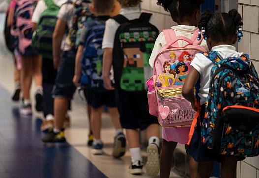 Kindergarteners walk down a hallway at school.