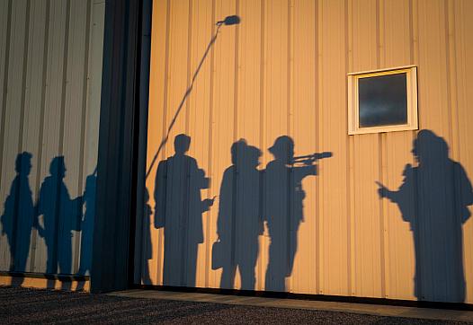 Silhouette of reporters shown against the wall of a hangar. 