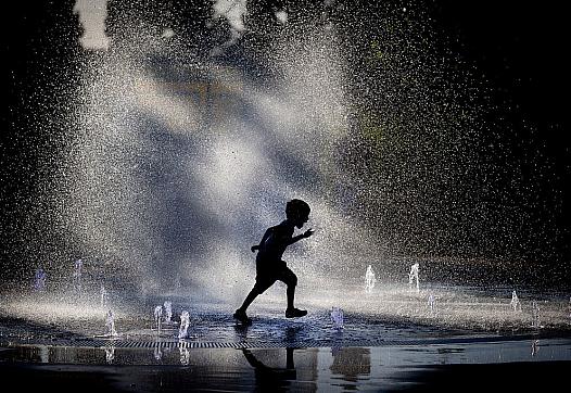 A young boy runs through a fountain.