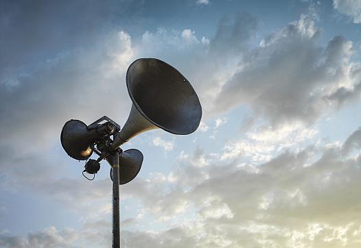 A loudspeaker silhouetted against a cloudy sky.
