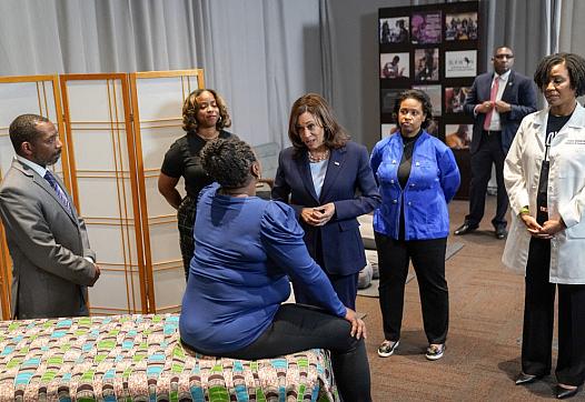 Person seated on a bed talking someone surrounded by people