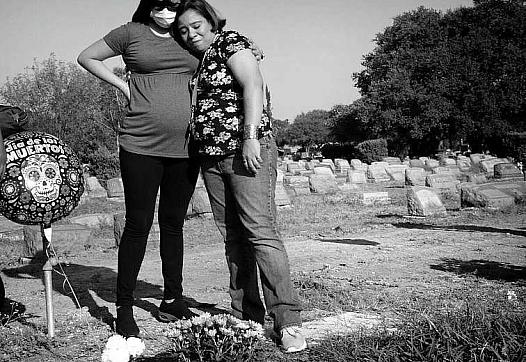 Two family members visit a grave in a cemetary.
