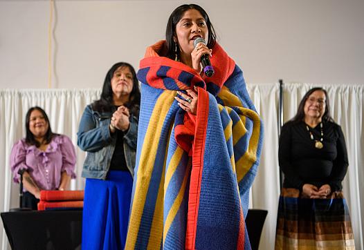 Huwighurruk Tribal Health Program graduate Desirae Barragan, wrapped in a colorful blanket, introduces herself in her native language during the Huwighurruk blanket ceremony in 2025. 