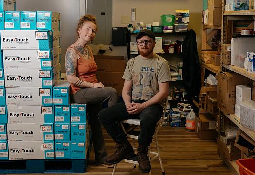 Two people sitting with a stack of needle boxes 