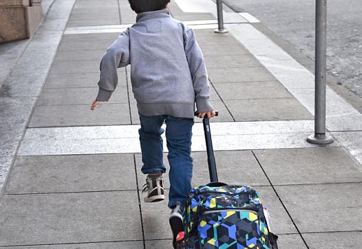 Young person running on a pavement dragging a bag with wheels