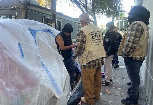 People in ERT (Encampment Resolution team) uniform around a guy near homeless shelter