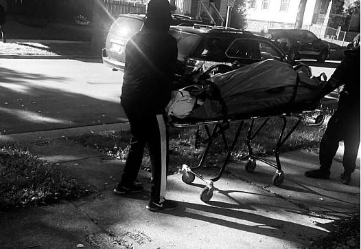 Black and white image of two people with Corpse on a stretcher.