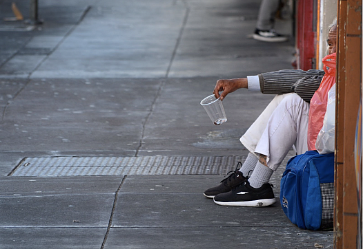 Person sitting on a sidewalk holding a cup 