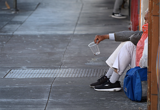 Person sitting on a sidewalk holding a cup