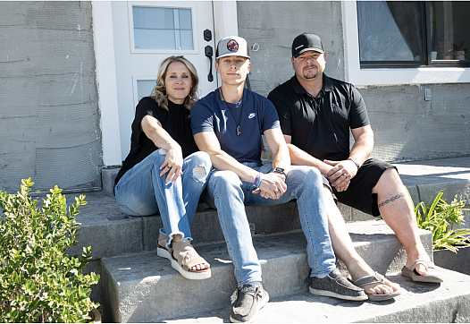 3 people seated on stairs in front of a door