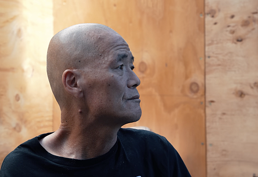 An older balding Korean man sits in profile inside a community shelter in Los Angeles
