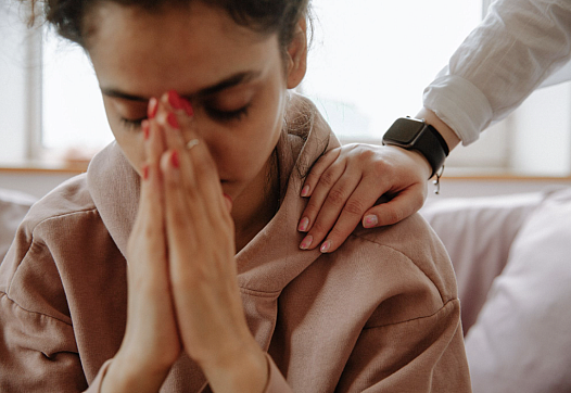 A young South Asian Indian Woman buries her face in her hands as a therapist comforts her.