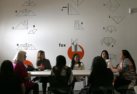 A meeting being held in a room with people seating across a table