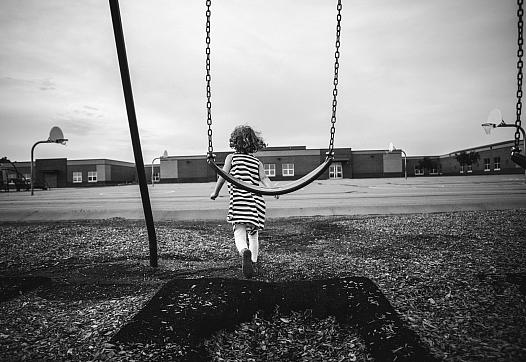 Black and white picture of a child walking away from a swing