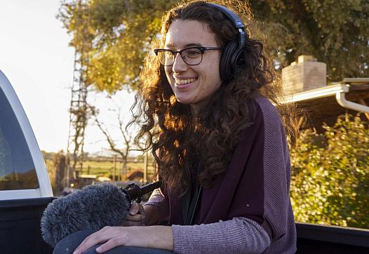 Image of a person holding mic and wearing headphones smiling