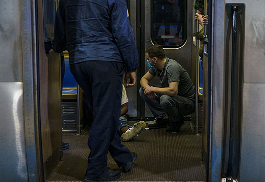 Person squatting in a train next to another person