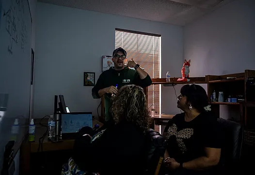 A man leads a discussion in a dimly lit office as two women listen.