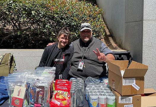 Two people posing with soda cans, chips, and other items