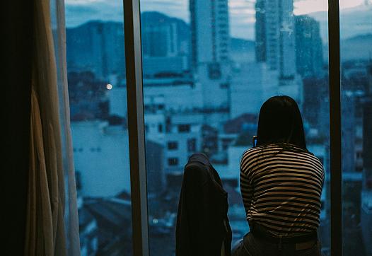 A woman stares out an apartment window.