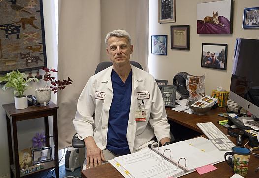 Person sitting on a desk in white lab coat with a folder open in front of him
