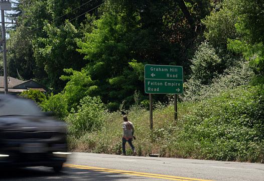 Car zooming through a road with greenery in the background and a person walking