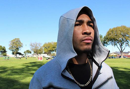 Abraham Jarvis, 18, poses for a photo at John F. Kennedy Park in San Diego on Feb. 10, 2023. Last year when Jarvis was 17, he was ticketed and briefly detained in the back of a police car for “switching lanes,” one example he says of him experiencing racial profiling. While being photographed, two police cars were parked in the distance. (Anissa Durham/Word In Black)