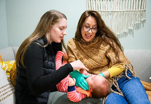 Person holding an infant and another women looking at the infant playfully