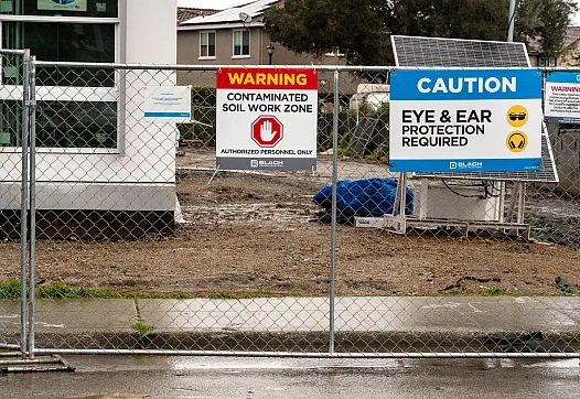 Warning signs posted on a fence at a construction site.