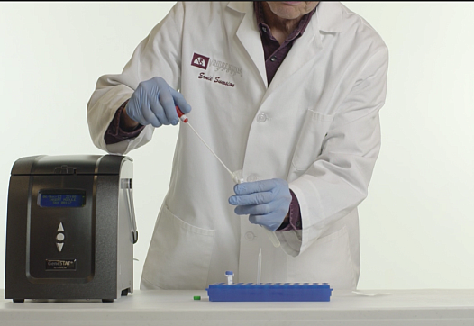 A lab technician works with a cocci sample to be used in a new testing instrument developed by DxNA LLC. that promises rapid, accurate detection.The specimen would be inserted into the machine, pictured to the left, and a diagnosis would be determined in about two hours. CREDIT: DxNA LLC