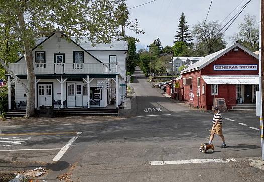 Man walking a dog past a general store in a quiet small town.
