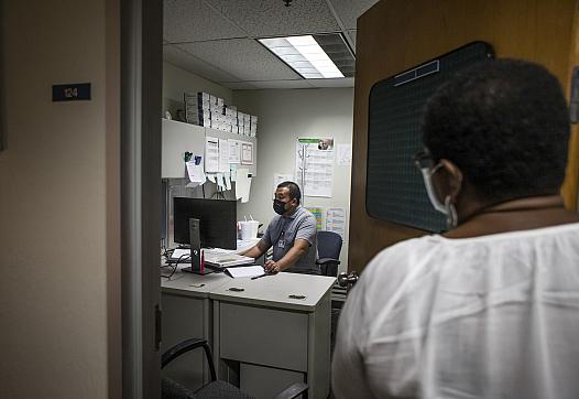 STD Investigator Hou Vang (left) works in his office as Jena Adams (right), Communicable Disease Program manager, checks in on h