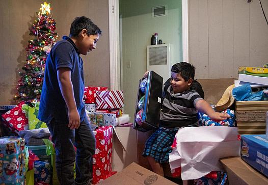Fernando Martinez, 10, left, watches his brother, Jonathan Sanchez Jr., 6, open shiny sport balls after gifts were brought to th