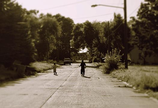 two children walking in the street between trees