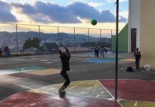 A Carver Elementary School student plays tetherball on the schoolyard at sunset with a staffer from the after-school program.