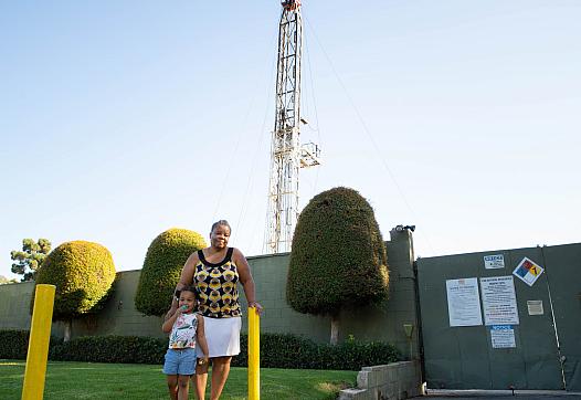 Deborah Bell-Holt and her granddaughter stand near an oil drilling site by her South Los Angeles home. A growing body of science